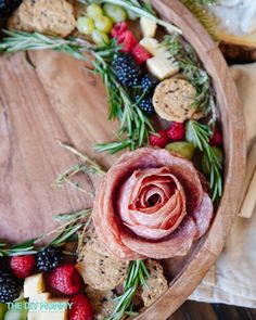 a wooden platter filled with meat, cheese and fruit on top of a table