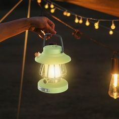 a person holding a green lantern in their hand at night with string lights hanging from the ceiling