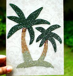 a hand holding up a card with beaded palm trees on it