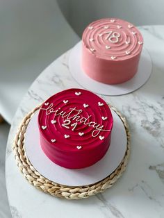 two birthday cakes sitting on top of a white table with pink frosting and hearts