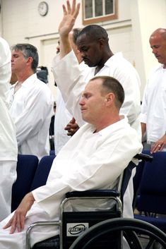 a man in a wheel chair with other men standing around him and clapping at the same time