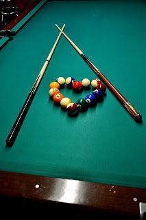 billiards balls and cues on a pool table with the cues in position