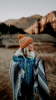 a woman wearing a blue jean jacket and orange knitted pom - pom hat