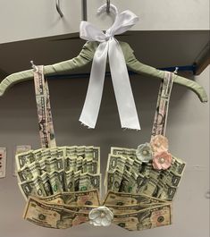 a money bra hanging on a hanger with white ribbon and flower decorations attached to it