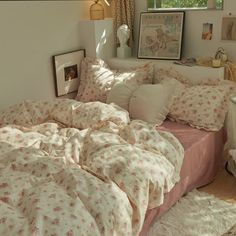 an unmade bed with pink and white comforter in a bedroom next to a window