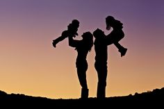 the silhouette of two people and a child against a purple sky at sunset or dawn