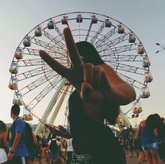 a person making the peace sign with their hand in front of a large ferris wheel