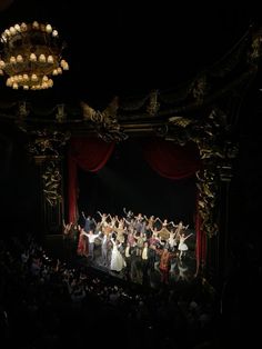 a group of people standing on top of a stage next to a chandelier