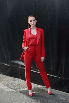 a woman standing in front of a black wall wearing red pants and a red jacket