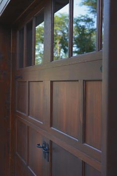 a close up of a wooden door with windows on the side of it and trees in the background