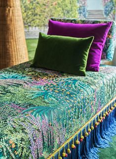 a bed covered in green and purple sheets with tassels on the bottom edge