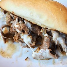 a close up of a sandwich on a plate with meat and cheese covered in gravy