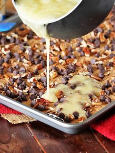 someone pouring batter onto a pan filled with chocolate chip cookie dough and toppings on top