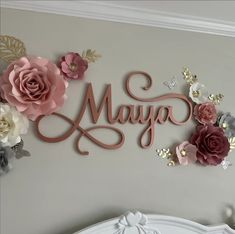 the word may spelled with pink and white flowers on a gray wall above a bed