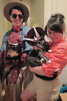 a man and woman holding two dogs wearing costumes