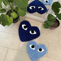 three blue heart shaped rugs with eyes on the floor next to potted plants