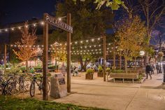 people are walking around in the park at night with lights strung over them and bicycles parked on the sidewalk