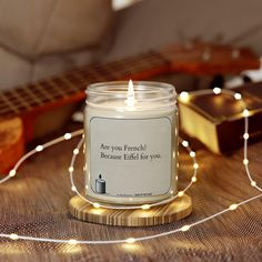 a lit candle sitting on top of a wooden table next to a guitar and string lights