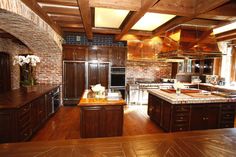 a large kitchen with wooden floors and brick walls, along with an island in the middle