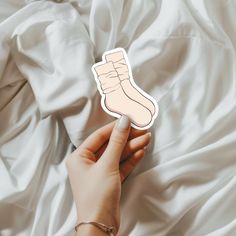 a hand holding a sticker with a foot on it in front of a white sheet