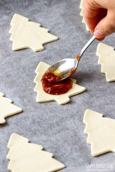 someone is spooning out some sauce on top of small christmas tree shaped cookies that are sitting on a baking sheet