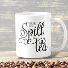 a white coffee mug with the words time to spill the tea on it next to some coffee beans