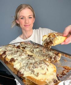 a woman is taking a piece of pizza out of the baking pan and it's ready to be eaten