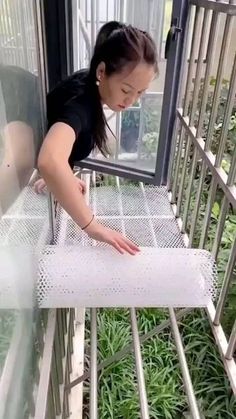 a woman standing on top of a window sill in front of a metal fence