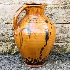 a brown and black vase sitting on top of a cement floor next to a brick wall