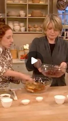 two women are preparing food in the kitchen and one is holding a bowl with something