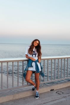 a woman standing next to the ocean with her legs crossed