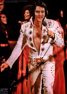 elvis presley singing into a microphone with other people in the background wearing red and white outfits