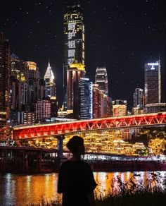 a man standing in front of a river with a city skyline behind him at night