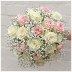 a bridal bouquet with baby's breath in front of a white brick wall