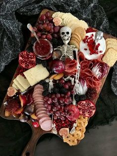 a wooden platter filled with cheese, crackers, fruit and skeleton figurines