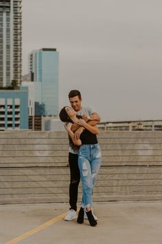 two people hugging each other while standing in front of some stairs with buildings in the background