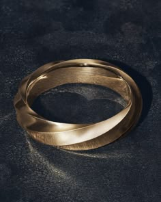 two gold wedding bands sitting on top of a black surface with one ring in the middle