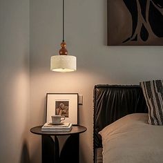 a lamp hanging over a bed next to a table with a cup on top of it