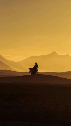 a person riding on the back of a horse across a desert field at sunset with mountains in the background