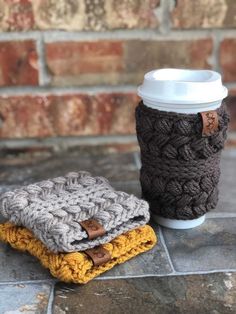 two coffee cups sitting next to each other on top of a stone floor near a brick wall