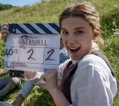 a young woman holding up a clapper in front of a movie set on the grass