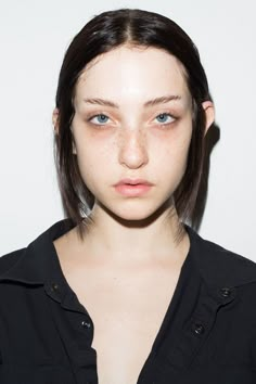 a young woman with freckles on her face looking at the camera while standing in front of a white background