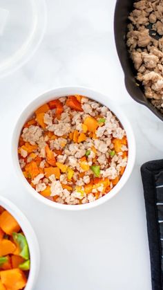 two bowls filled with food sitting on top of a white counter next to plates and utensils