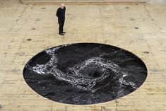 a man standing in front of a large black piece of art on top of a brick floor