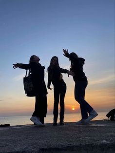 three women standing on the beach with their arms out in front of the sun setting