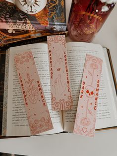 an open book with pink and red designs on it next to a vase filled with flowers