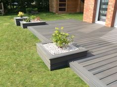 a wooden deck with plants and gravel in the middle on grass next to brick building