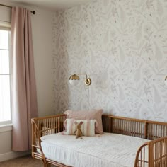 a baby's crib in front of a window with pink and white wallpaper