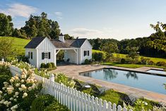 a white house with a pool in the yard and landscaping around it is surrounded by greenery