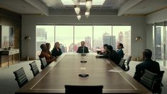 a group of people sitting at a conference table in front of large windows looking out onto the city